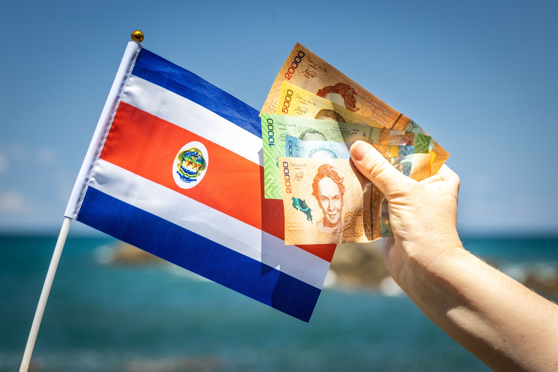 A woman holds money in her hand and the flag of Costa Rica against the background of the sea. Holiday travel and spending concept
